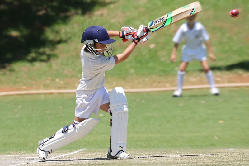 Young batter playing a shot on a sunny cricket ground